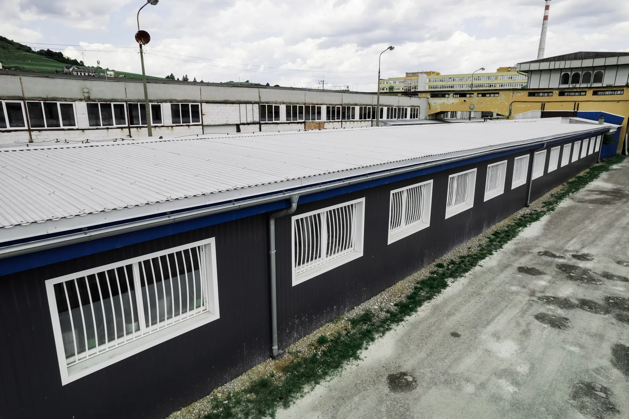 Trapézová plechová strecha aluzinok nad tmavou fasádou výrobnej haly v Nižnej