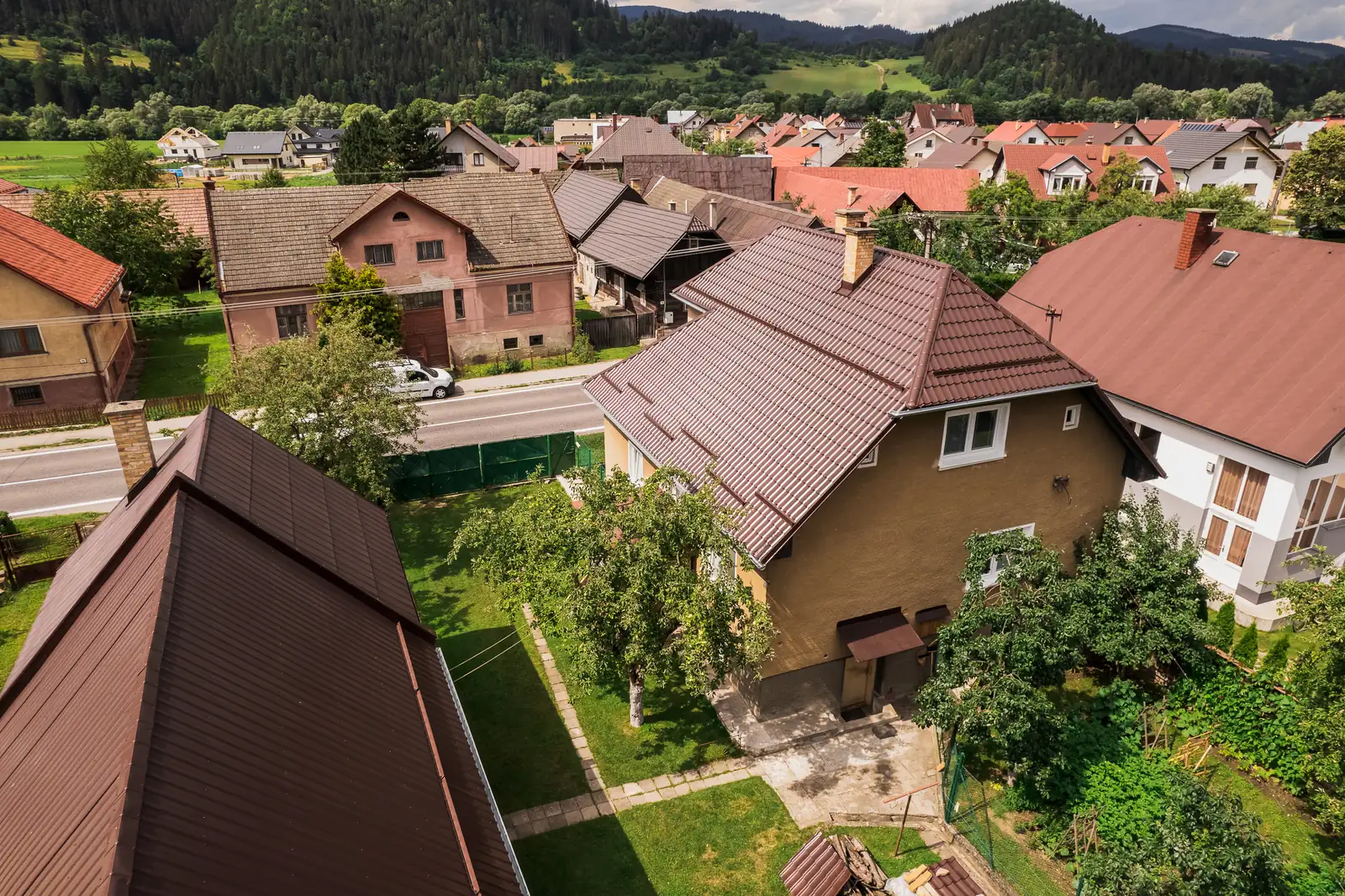 Rodinný dom so strechou z hnedého škridloplechu v zástavbe obce Krivá, pohľad z dronu
